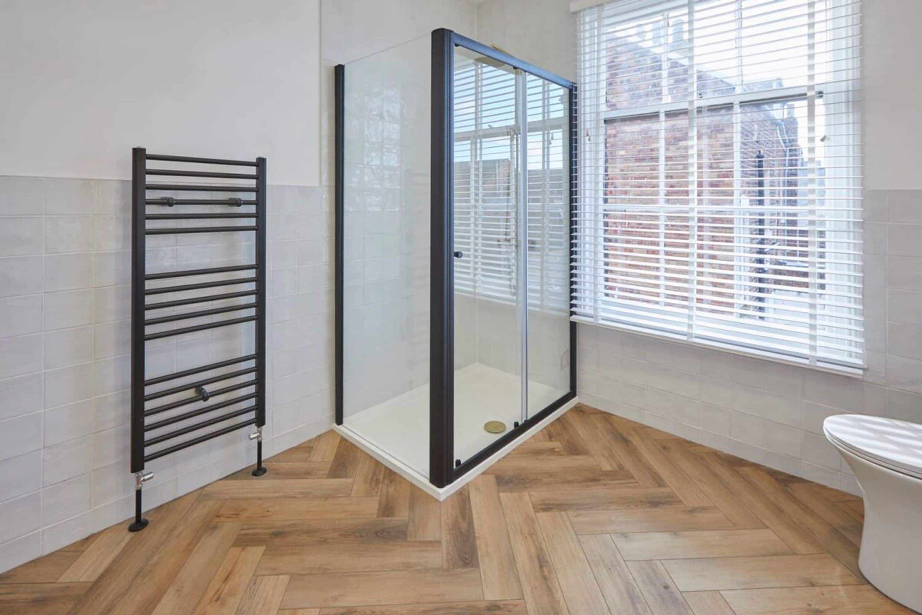 A bathroom with a glass shower enclosure, a black towel rack, and a toilet.
