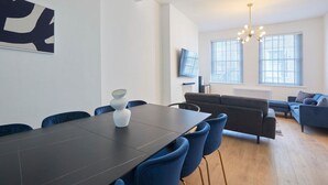 A modern living room with a dark wooden dining table, blue chairs, a grey sofa, and a TV mounted on the wall. - Host Stay Castle View (Scarborough)