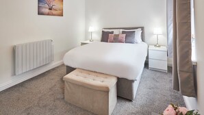 A hotel room with a large bed, two bedside tables with lamps, a radiator, and a painting on the wall. - Host Stay Britton Hall Bungalow (Bishop Auckland)