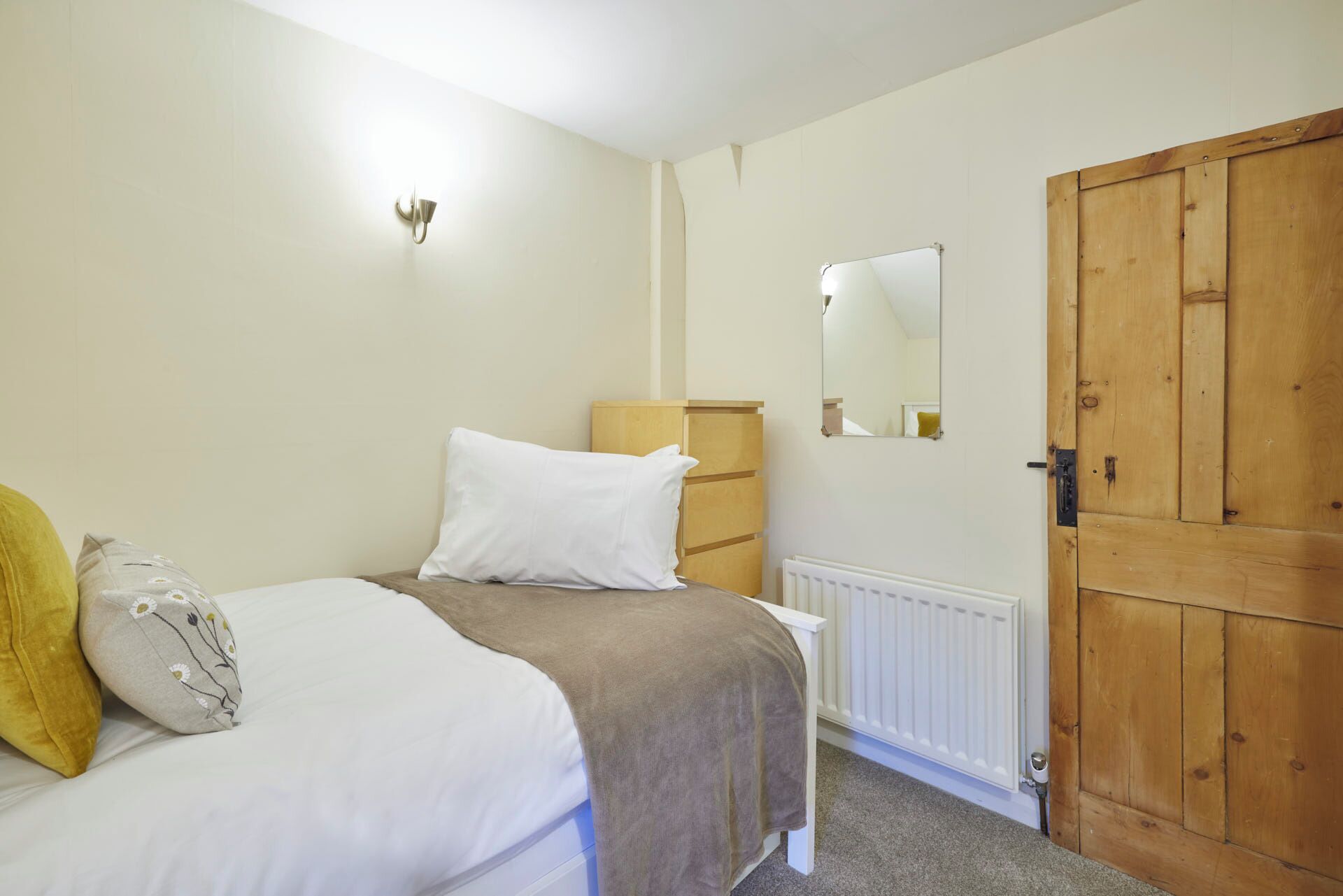 A bedroom with a bed, a wooden wardrobe, a radiator, and a wall-mounted light fixture.