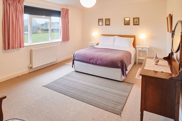 A bedroom with a bed, bedside tables, a dresser, a mirror, and a window with curtains.