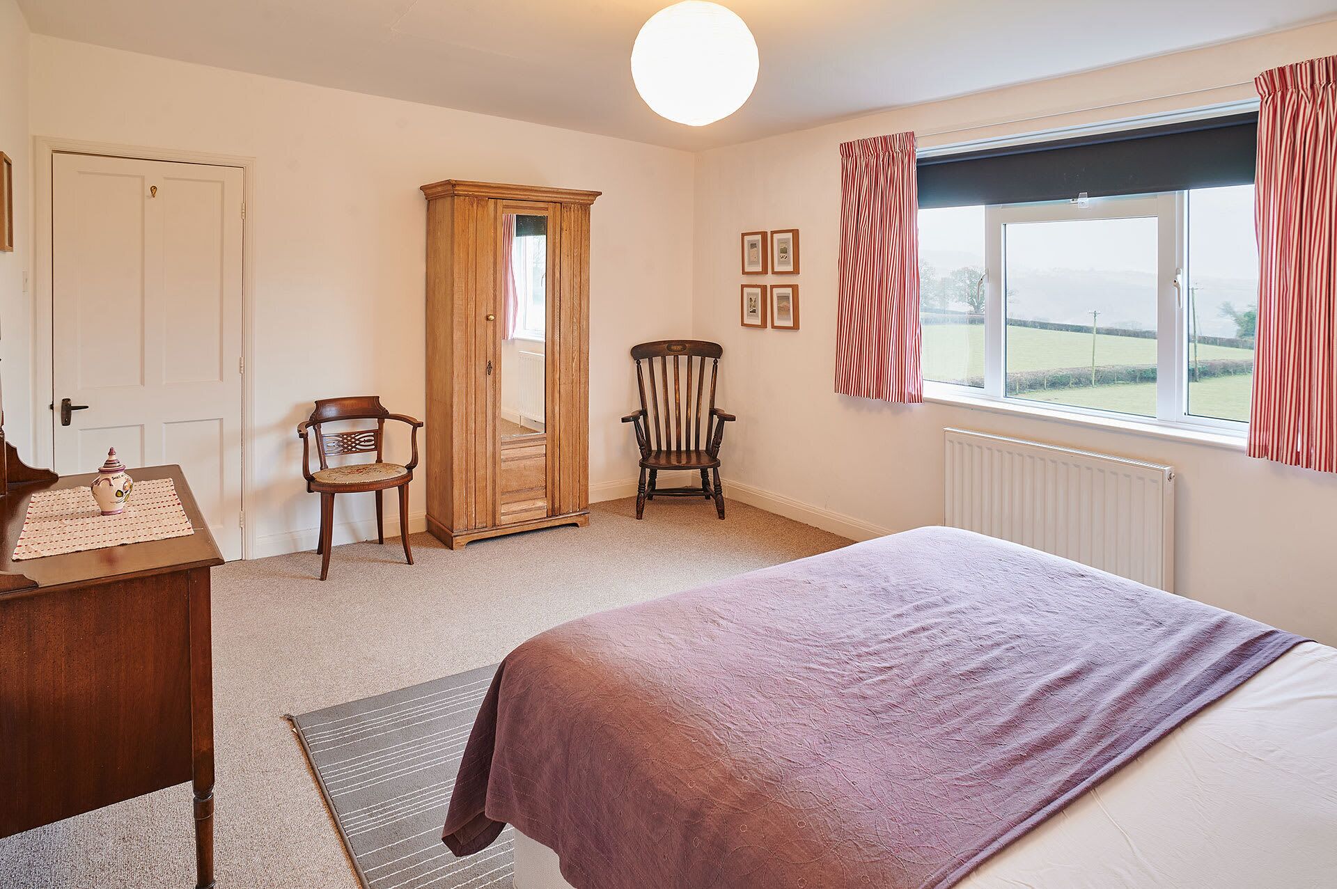 A bedroom with a bed, a wooden wardrobe, a chair, a radiator, and a window with curtains.