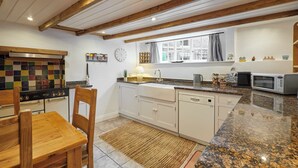 Una cocina con armarios blancos, encimera de granito, estufa, lavavajillas y una ventana con cortinas.