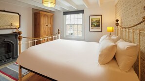 Una cama grande con ropa de cama blanca, un armario de madera, una chimenea y una ventana con vistas a edificios.