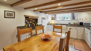 Una cocina con armarios de madera, salpicadero de azulejos, una mesa de comedor con sillas, microondas y una ventana con cortinas.