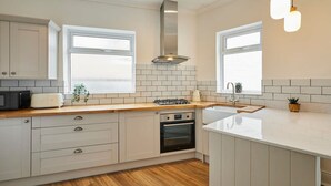 A modern kitchen with white cabinetry, a wooden countertop, a built-in oven, and a large window providing natural light. - Host Stay Sunbeam House (Saltburn-by-the-Sea)