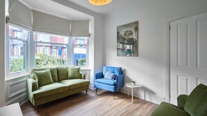A living room with a green sofa, a blue armchair, and a small white side table. - Host Stay Sunbeam House (Saltburn-by-the-Sea)