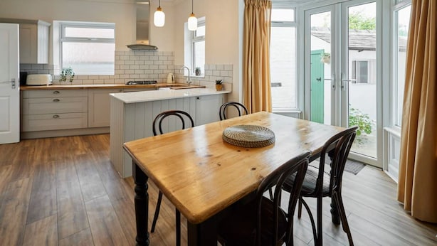 A modern kitchen with a wooden dining table, white cabinets, and a large window with curtains. - Host Stay Sunbeam House (Saltburn-by-the-Sea)