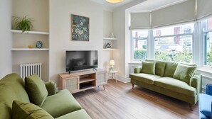 A living room with a green sofa, a TV on a wooden stand, and a window with a view of the outside. - Host Stay Sunbeam House (Saltburn-by-the-Sea)