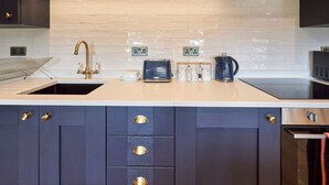 Una cocina moderna con armarios oscuros, una encimera blanca, un grifo dorado y un horno de acero inoxidable.