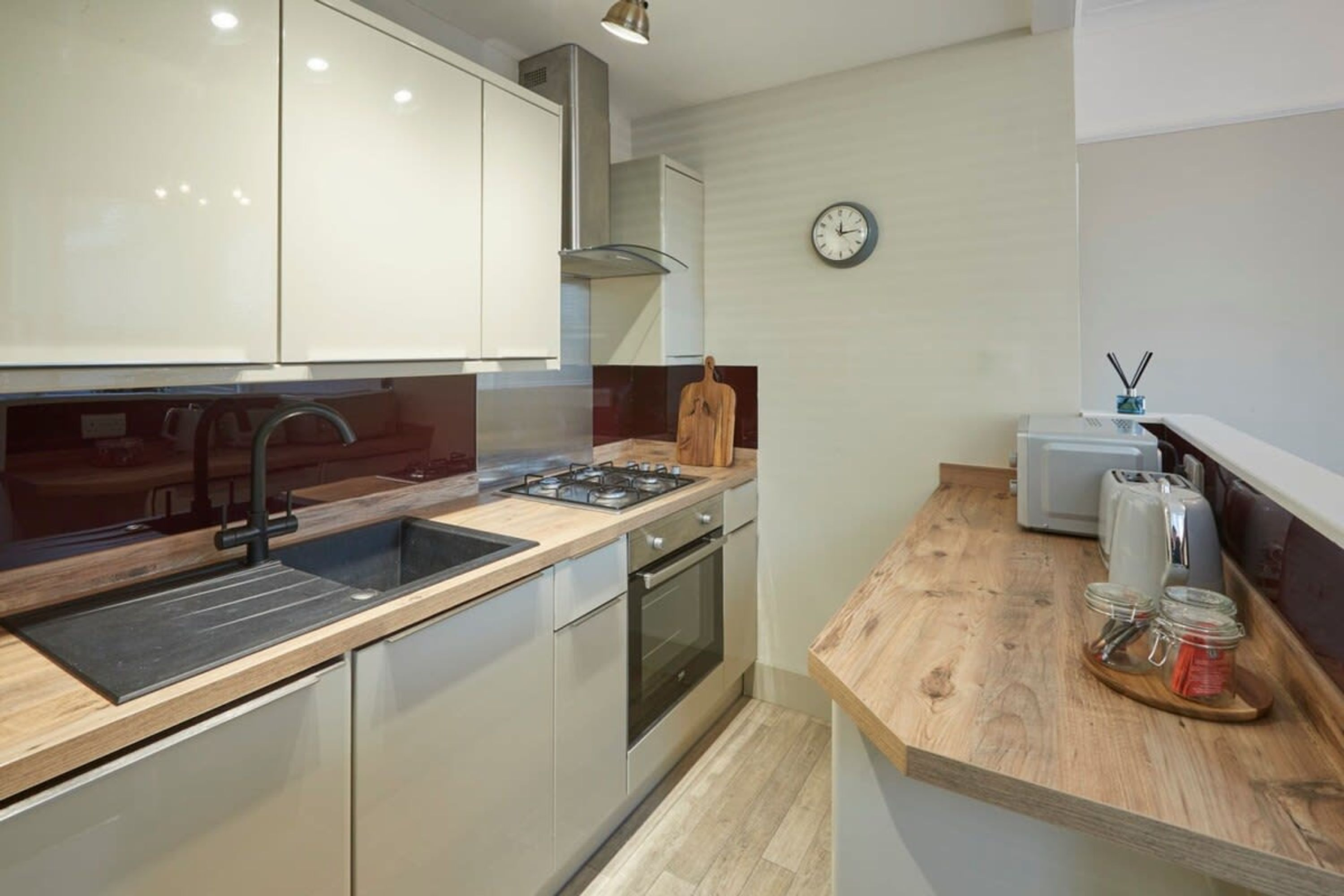 A modern kitchen with stainless steel appliances, a wooden countertop, and a wall clock.