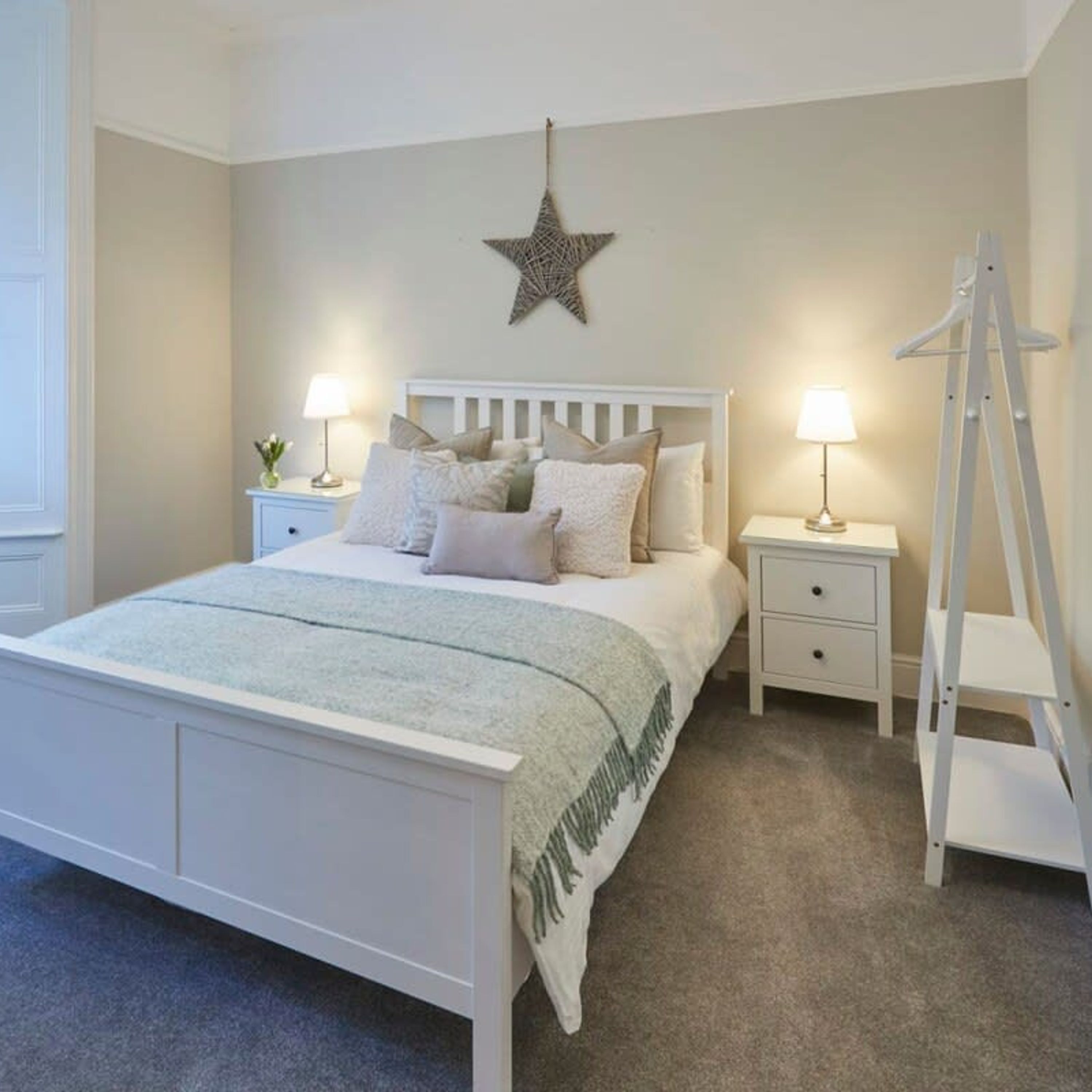 Une chambre avec un lit blanc, deux tables de chevet avec des lampes, une décoration en forme d’étoile sur le mur et une échelle blanche.