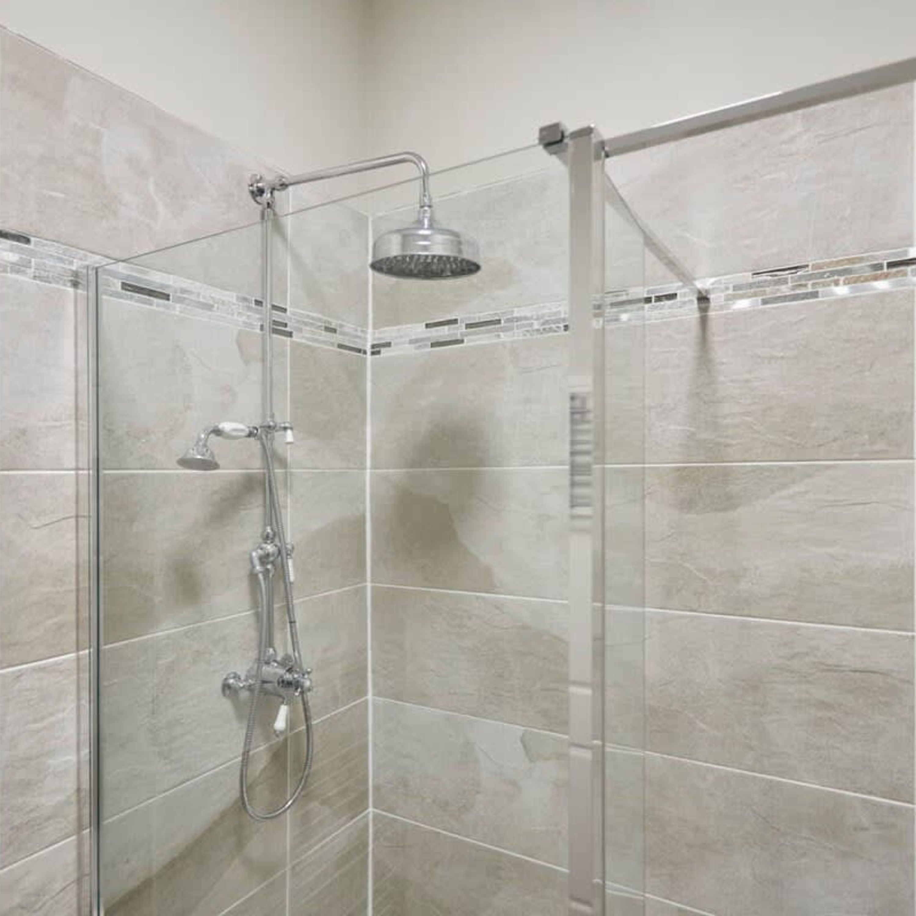A glass-enclosed shower with a handheld showerhead and a wall-mounted faucet.