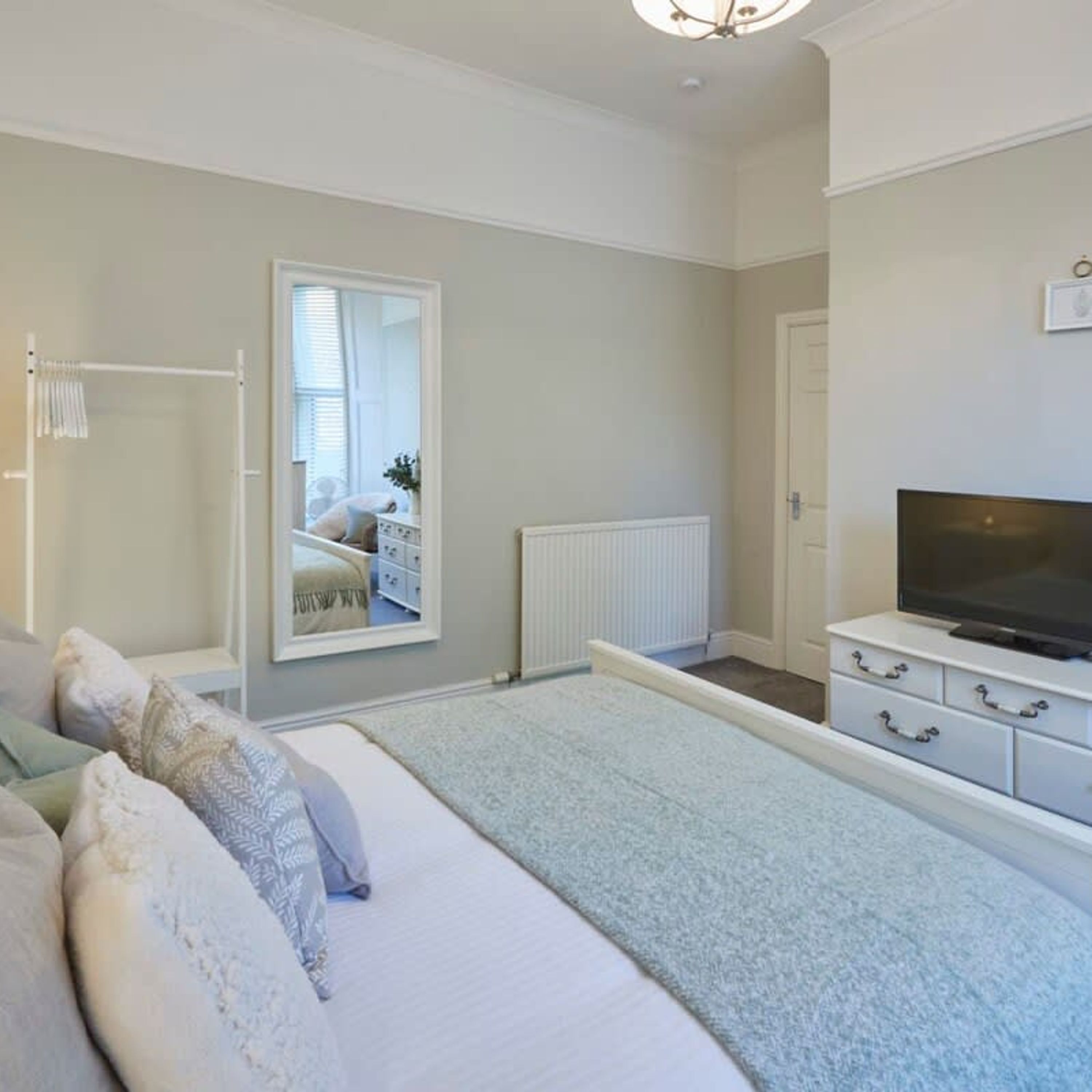 A bedroom with a bed, a television, a dresser, and a mirror.