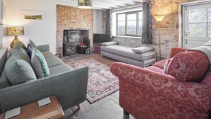 Ein gemütliches Wohnzimmer mit Kamin, einer Couch, einem roten Sessel und einem gemusterten Teppich.