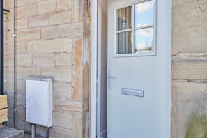 A door with a window, set against a stone wall, features a mounted electrical box.