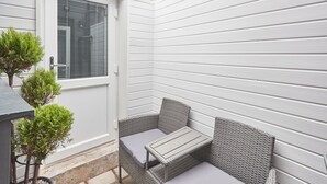 Un petit patio aménagé dans un coin, avec un canapé et une table en osier, une porte et deux petites plantes en pot.