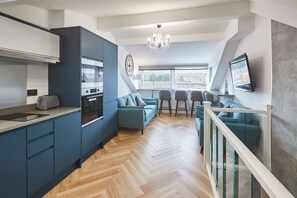 A modern kitchen with built-in appliances, a dining area with a view, and a staircase with glass railings. - Host Stay Wadsworth Cottage (Whitby)
