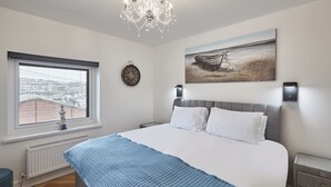 Une chambre avec un grand lit, une vue sur la ville par la fenêtre, une horloge au mur et un tableau au-dessus du lit.