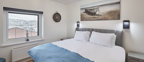 A bedroom with a large bed, a view of the city through a window, a clock on the wall, and a painting above the bed.