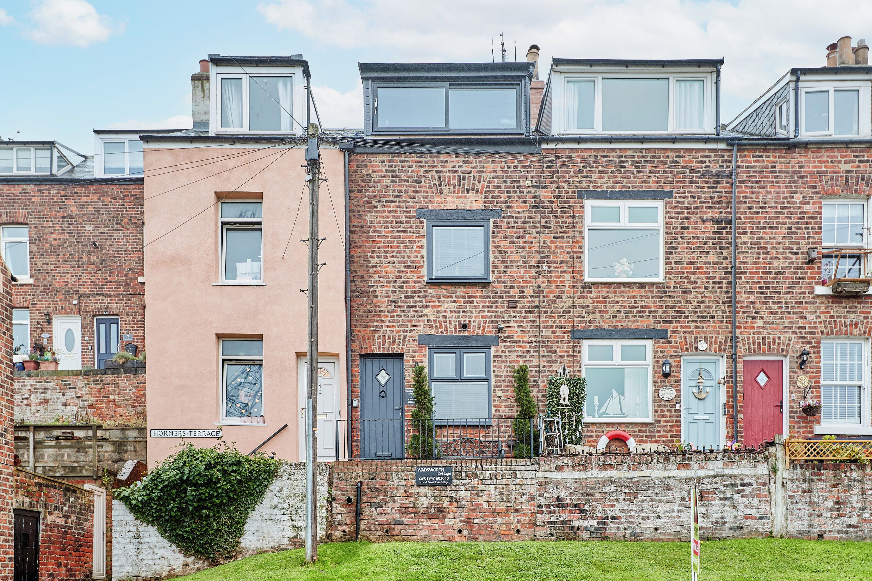 A row of terraced houses with brick facades, multiple windows, and a small garden area in front.