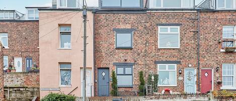 A row of terraced houses with brick facades, multiple windows, and a small garden area in front.