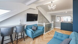 Un appartement moderne de style « loft », avec un plafond haut, un coin repas doté de tabourets de bar, un canapé et une cuisine avec fenêtre.