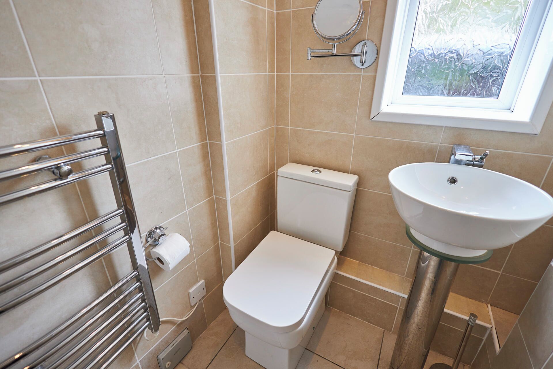 Un baño pequeño y moderno con inodoro, lavamanos de vidrio y un perchero para toallas.