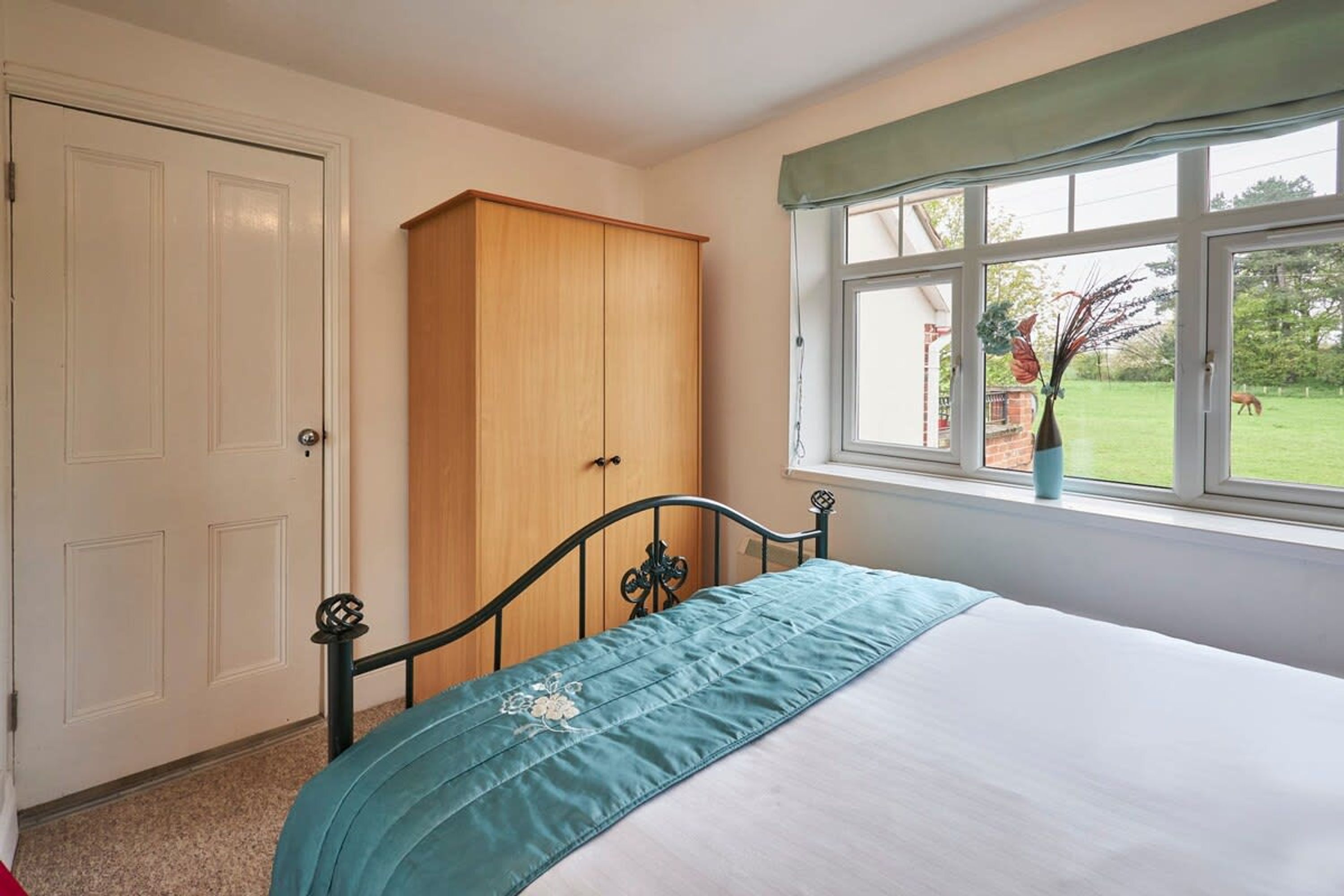 A bedroom with a bed, a wardrobe, and a window with a view of a garden.