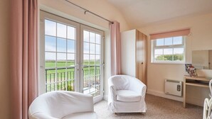 A room with two white chairs, a desk, a radiator, and a window with a view of a green field. - Host Stay The Paddock (Bedlington)