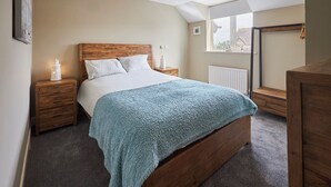 Et soveværelse med en træseng, et blåt tæppe, et natbord med en lampe og et vindue med udsigt til bygninger.