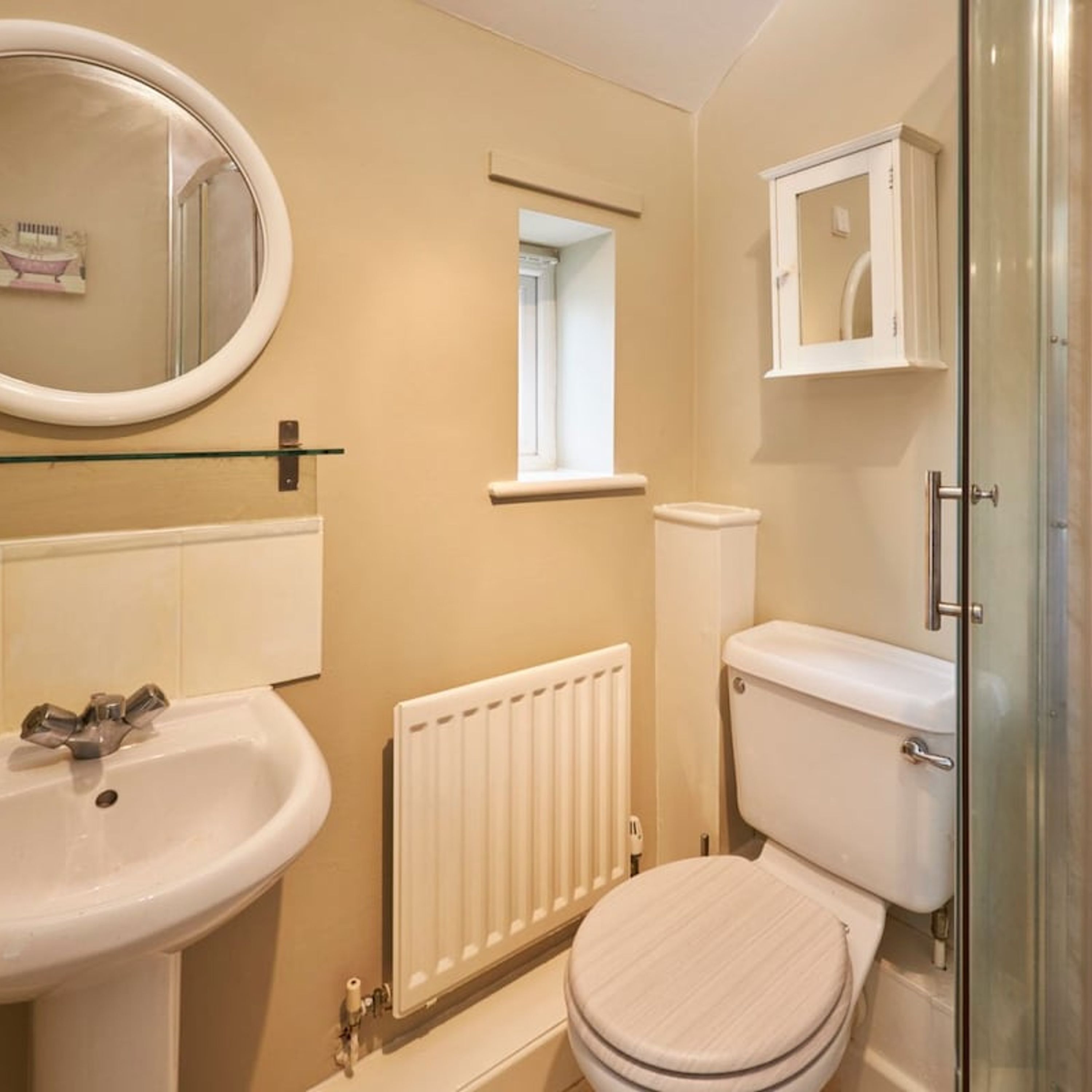 A bathroom with a white sink, a toilet, a glass shower enclosure, and a window above the toilet.