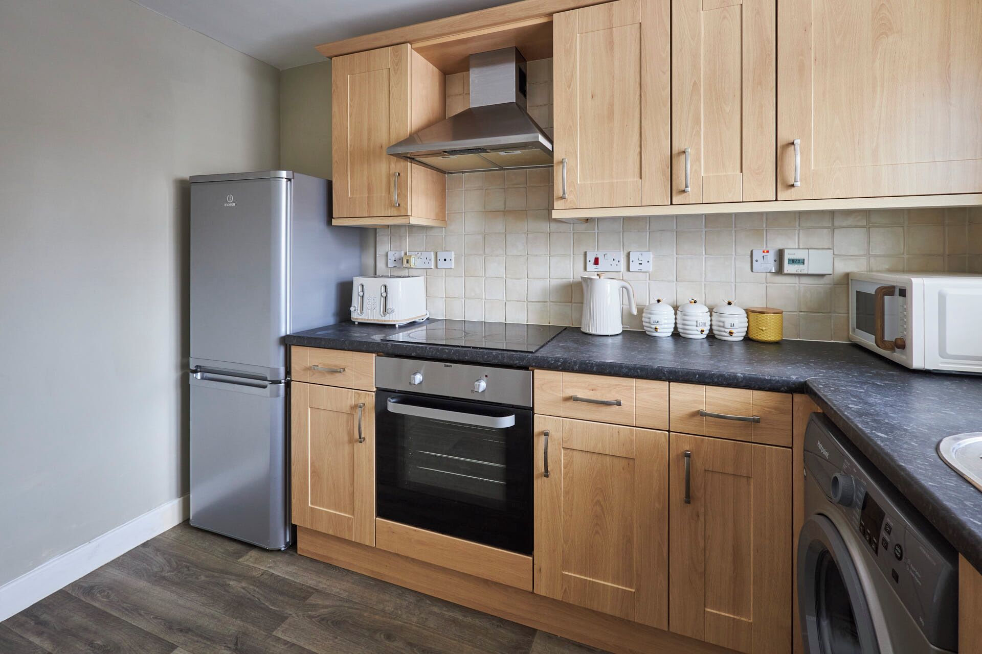 Una cocina moderna con armarios de madera, un refrigerador de acero inoxidable, un horno empotrado, un microondas y una lavadora.