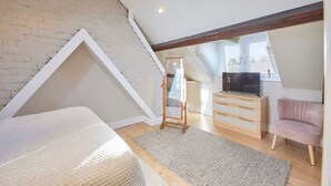 A loft bedroom with a sloped ceiling, a wooden dresser, a television, a pink chair, and a mirror. - Host Stay The Cottage in Corbridge (Corbridge)