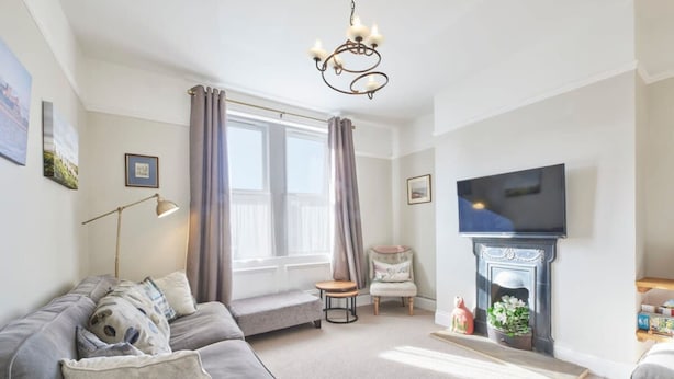 A living room with a grey sofa, a small table, a chair, a fireplace, and a television mounted on the wall. - Host Stay The Cottage in Corbridge (Corbridge)