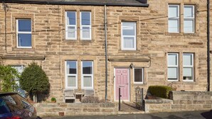 A stone-built terraced house with a pink door, multiple windows, and a small front garden. - Host Stay The Cottage in Corbridge (Corbridge)