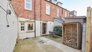 A courtyard with a brick building, a white door, a wooden shed, and a table with chairs. - Host Stay The Cottage in Corbridge (Corbridge)