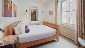 Ein Schlafzimmer mit einem hölzernen Bett, einem Nachttisch, einem Spiegel, einem Fenster mit Vorhängen und Bildern an den Wänden.