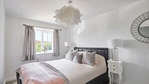 Un dormitorio con cama, lámpara de noche, ventana con cortinas y un espejo adosado a la pared.