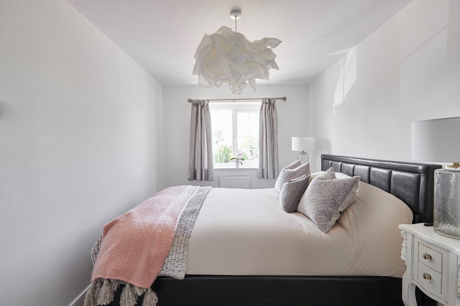 A bedroom with a bed, bedside table, lamp, and a window with curtains.