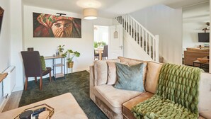 Una sala de estar con un sofá, una mesa de centro, un cuadro en la pared, una escalera y un área de comedor al fondo.