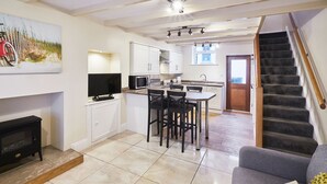 Een moderne keuken met witte kasten, een eethoek met zwarte stoelen, en een trap naar een hoger niveau.