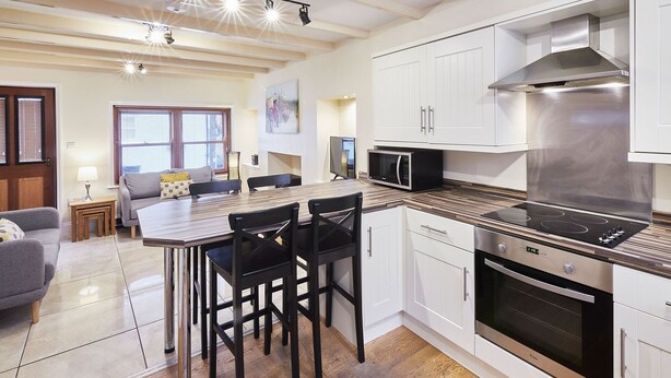 Een moderne keuken met witte kastjes, een zwarte kookplaat en een eethoek met een houten tafel en stoelen.