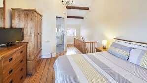 Een slaapkamer met een houten dressoir, een bed met beddengoed met een patroon, een nachtkastje met een lamp en uitzicht op de badkamer.