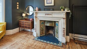A room with a fireplace, wooden flooring, a yellow chair, a dresser, and a mirror. - Host Stay Northville Arrifana (Whitley Bay)