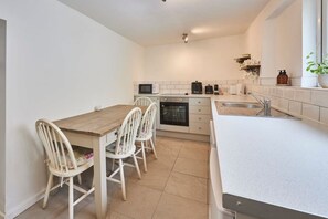 A compact kitchen with a wooden table and chairs, a microwave, a coffee maker, and a sink. - Host Stay Daisy s Cottage (Hexham)