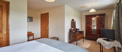 A bedroom with a large bed, a dresser, a mirror, a television, and a wardrobe.