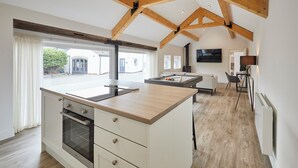 A modern kitchen with wooden beams, a large island, and a view of the outside. - Host Stay The Hay Loft (Wakefield)