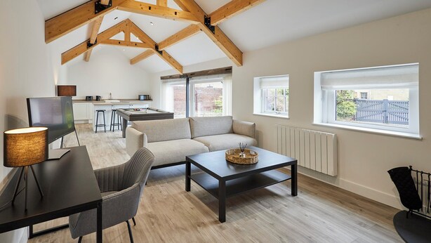 A spacious living area with a high ceiling, a sofa, a coffee table, and a TV. - Host Stay The Hay Loft (Wakefield)