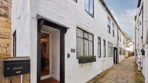 A narrow street with white buildings, a wooden post box labeled "POST", and a door leading to a room. - Host Stay Cragg Cottage (Whitby)